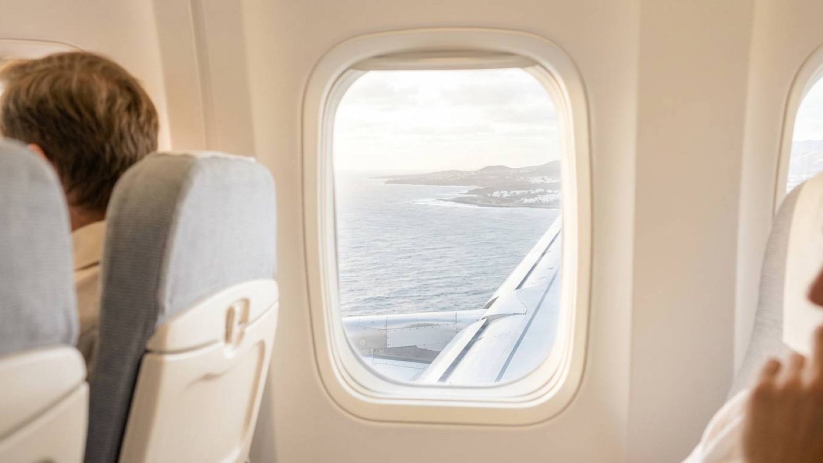 The view of a sunlit coastline through an aircraft window from inside the cabin