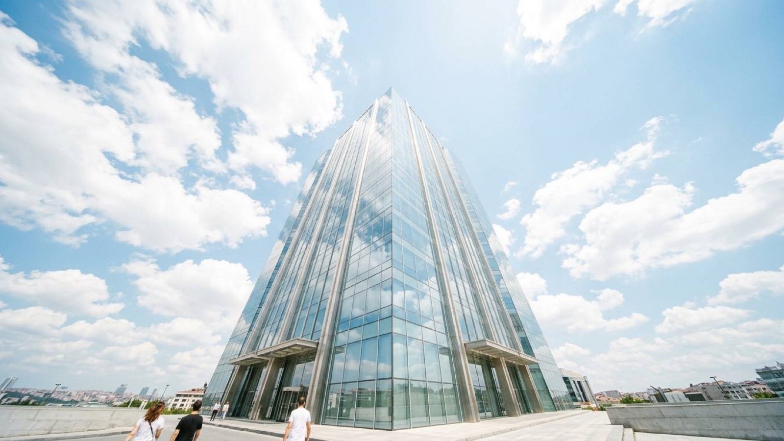 A glass office tower seen from street level against a bright sky