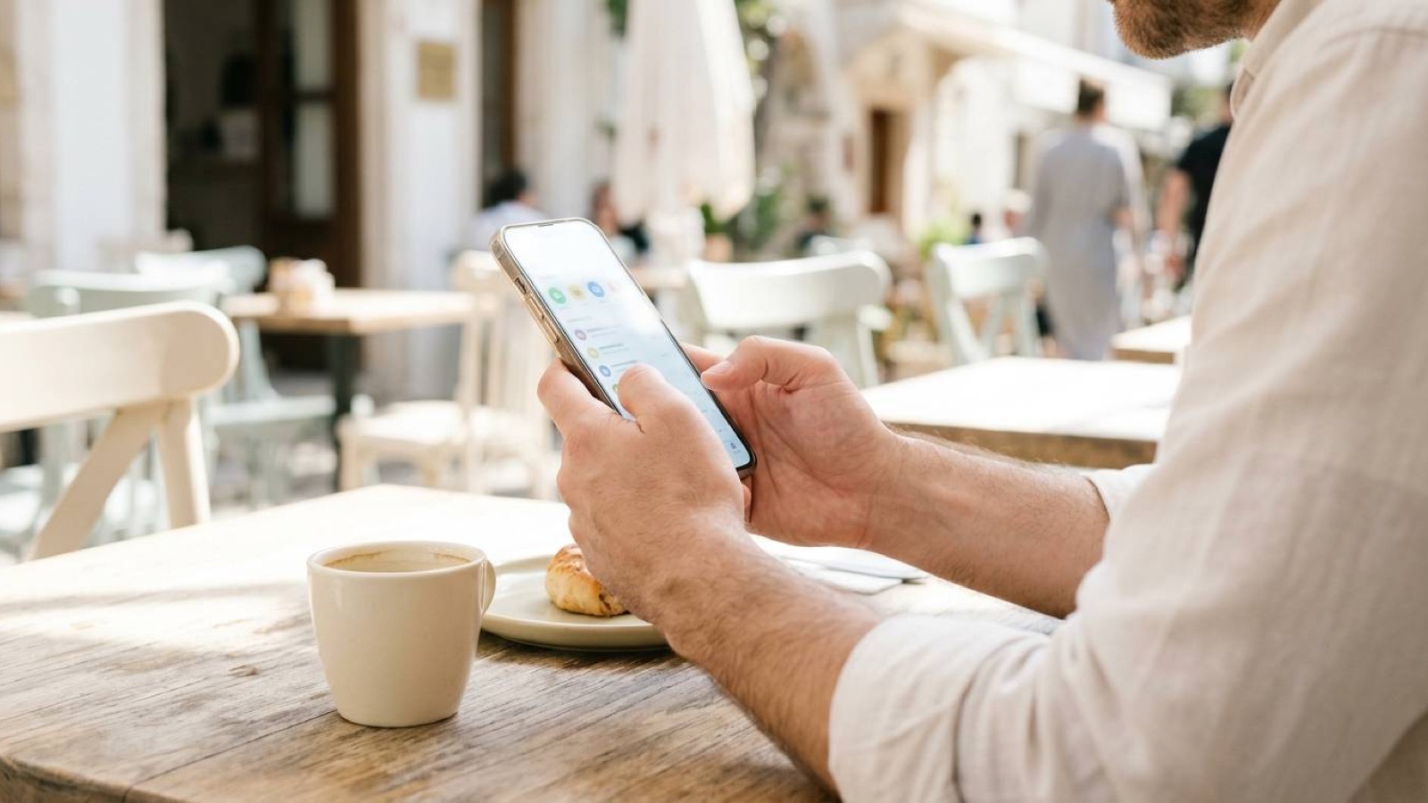 A man using a smartphone at a sunlit outdoor cafe table
