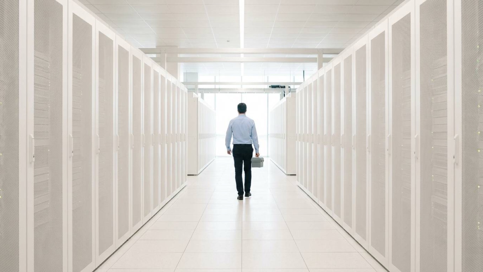 A technician walking away down an aisle of white server racks in a data centre