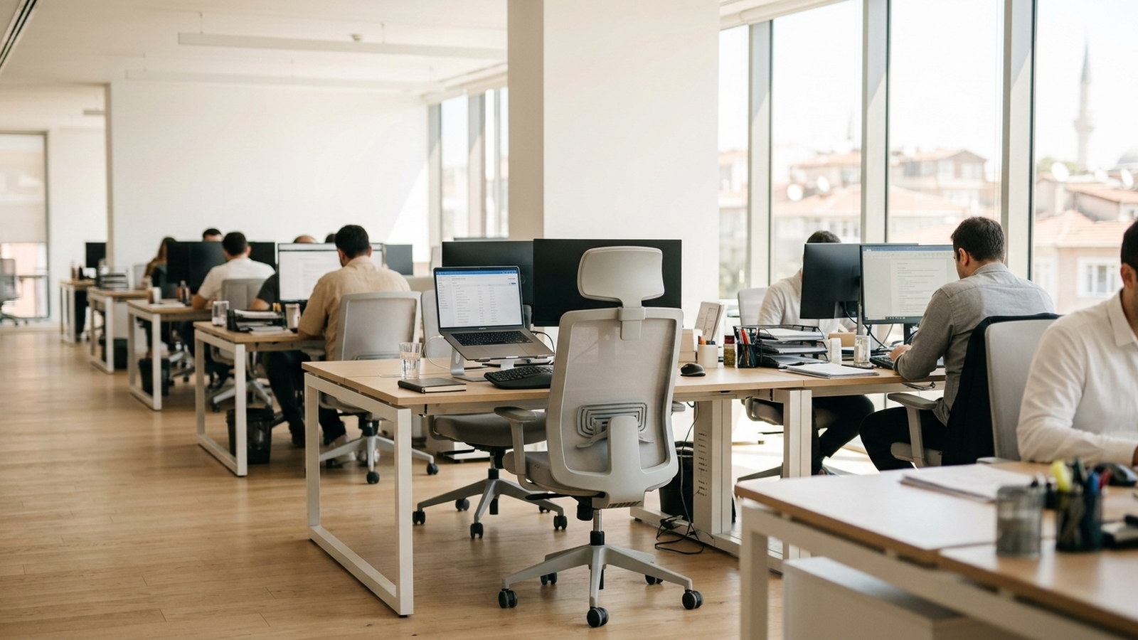 An empty desk chair at a fully set up workstation in a busy Istanbul office, colleagues working at the desks either side